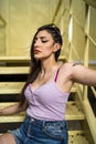 Young rebellious caucasian female with tattoos and in jeans skirt posing while sitting on the stairs