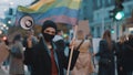 Young rebellious woman with face mask and megaphone holding rainbow flag in crowd. Protest against discrimination