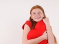 Young red hair girl tenderly hug a heart shape on grey background