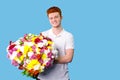 Young red hair man happy holding a big beautiful bouquet of flowers in his hands over blue background, copy space. Royalty Free Stock Photo
