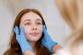 A young red-haired beautiful girl undergoes a medical examination in a cosmetology clinic. A female dermatologist