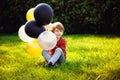 Young red-haired boy playing with a bunch of yellow white black balloons in the Park Royalty Free Stock Photo