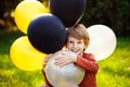 Young red-haired boy playing with a bunch of yellow white black balloons in the Park Royalty Free Stock Photo