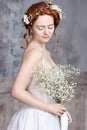 Young red-haired bride in elegant white wedding dress. She stands, her eyes are dreamy closed,