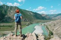 A young red-haired girl in a blue t-shirt with a backpack stands on a rock and looks towards the Katun river in the Altai Royalty Free Stock Photo