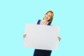 A young red-haired girl is holding a large white poster or piece of paper posing at the camera with a smile on an Royalty Free Stock Photo