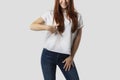 Young red-haired girl isolated on gray background in white t-shirt. She points her finger down