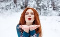 Young red-haired girl with long red hair on a winter background.Air kiss. Red-haired woman in a summer dress on the background of Royalty Free Stock Photo