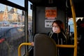 A young red-haired girl in a medical mask rides to work in a city bus.