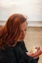 Young red-haired girl sits on a fishing net and looks at a seashell in her hands Royalty Free Stock Photo