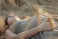 Young red-haired happy woman lying on wheat field in summer at sunset touching belly, future mother relaxing on nature, healthy Royalty Free Stock Photo