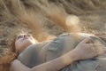Young red-haired happy woman lying on wheat field in summer at sunset touching belly, future mother relaxing on nature, healthy Royalty Free Stock Photo
