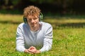 Young red-haired man in headphones lies on the green grass Royalty Free Stock Photo