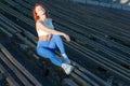 Young red-haired sportswoman sits on a wooden bench of a sports stadium in the rays of the setting sun. on a dark