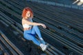 Young red-haired sportswoman sitting on a wooden bench of a sports stadium, in the beam of the setting sun. on a dark background.