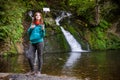 Young woman blogger in autumn mountains near lake and waterfall is recording video, taking photo with selfie stick Royalty Free Stock Photo