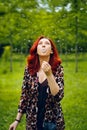 Young red-haired woman blows away a dandelion.