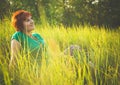 Young red-haired woman sitting in the grass and enjoying sunny summer day. Portrait of happy smiling young girl in nature Royalty Free Stock Photo