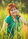 Young red-haired woman sitting in the grass and enjoying sunny summer day. Portrait of happy smiling young girl in nature Royalty Free Stock Photo