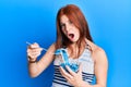 Young red head girl eating measure meter doing diet for weight loss afraid and shocked with surprise and amazed expression, fear Royalty Free Stock Photo