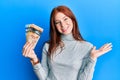 Young red head girl holding canadian dollars celebrating achievement with happy smile and winner expression with raised hand