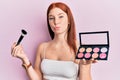 Young red head girl holding makeup brush and blush palette looking at the camera blowing a kiss being lovely and sexy Royalty Free Stock Photo