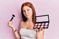 Young red head girl holding makeup brush and blush palette skeptic and nervous, frowning upset because of problem Royalty Free Stock Photo