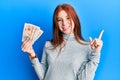 Young red head girl holding 10 united kingdom pounds banknotes smiling happy pointing with hand and finger to the side