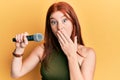 Young red head girl singing song using microphone covering mouth with hand, shocked and afraid for mistake Royalty Free Stock Photo