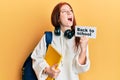 Young red head girl wearing backpack holding back to school banner angry and mad screaming frustrated and furious, shouting with