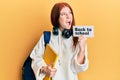 Young red head girl wearing backpack holding back to school banner angry and mad screaming frustrated and furious, shouting with Royalty Free Stock Photo