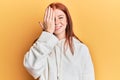 Young red head girl wearing casual sweatshirt covering one eye with hand, confident smile on face and surprise emotion Royalty Free Stock Photo