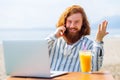 young redhaired ginger bearded man working outdoors in sea cafe with laptop an summer day