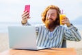 young redhaired ginger bearded man working outdoors in sea cafe with laptop an summer day