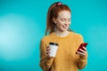 Young redhaired woman with coffee and smartphone isolated over b