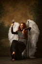 Young redhaired woman drinking wine while sitting dressed like warrior knight and holds sword against vintage studio Royalty Free Stock Photo