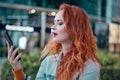 Young redhaired woman  standing at night with phone by european skyline Royalty Free Stock Photo