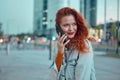 Young redhaired woman standing at night with phone by european skyline