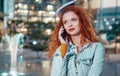 Young redhaired woman standing at night with phone by european skyline