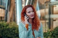 Young redhaired woman standing at night with phone by european skyline