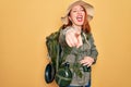 Young redhead backpacker woman hiking wearing backpack and hat over yellow background laughing at you, pointing finger to the Royalty Free Stock Photo