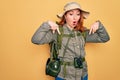 Young redhead backpacker woman hiking wearing backpack and hat over yellow background Pointing down with fingers showing Royalty Free Stock Photo