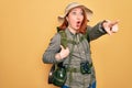 Young redhead backpacker woman hiking wearing backpack and hat over yellow background Pointing with finger surprised ahead, open Royalty Free Stock Photo
