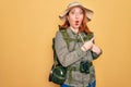 Young redhead backpacker woman hiking wearing backpack and hat over yellow background Surprised pointing with finger to the side, Royalty Free Stock Photo