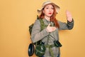 Young redhead backpacker woman hiking wearing backpack and hat over yellow background Swearing with hand on chest and open palm, Royalty Free Stock Photo