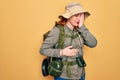 Young redhead backpacker woman hiking wearing backpack and hat over yellow background Yawning tired covering half face, eye and