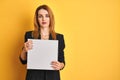 Young redhead businesswoman with clear eyes holding banner over isolated yellow background with a confident expression on smart