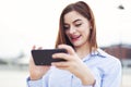 Young redhead businesswoman messaging by smartphone and laughing outdoors