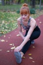 Young redhead woman leg stretching warm up before running on track at autumn Royalty Free Stock Photo