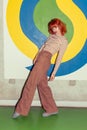 Young redhead Caucasian woman in retro style of 70s posing at wall full body and looking into camera Royalty Free Stock Photo